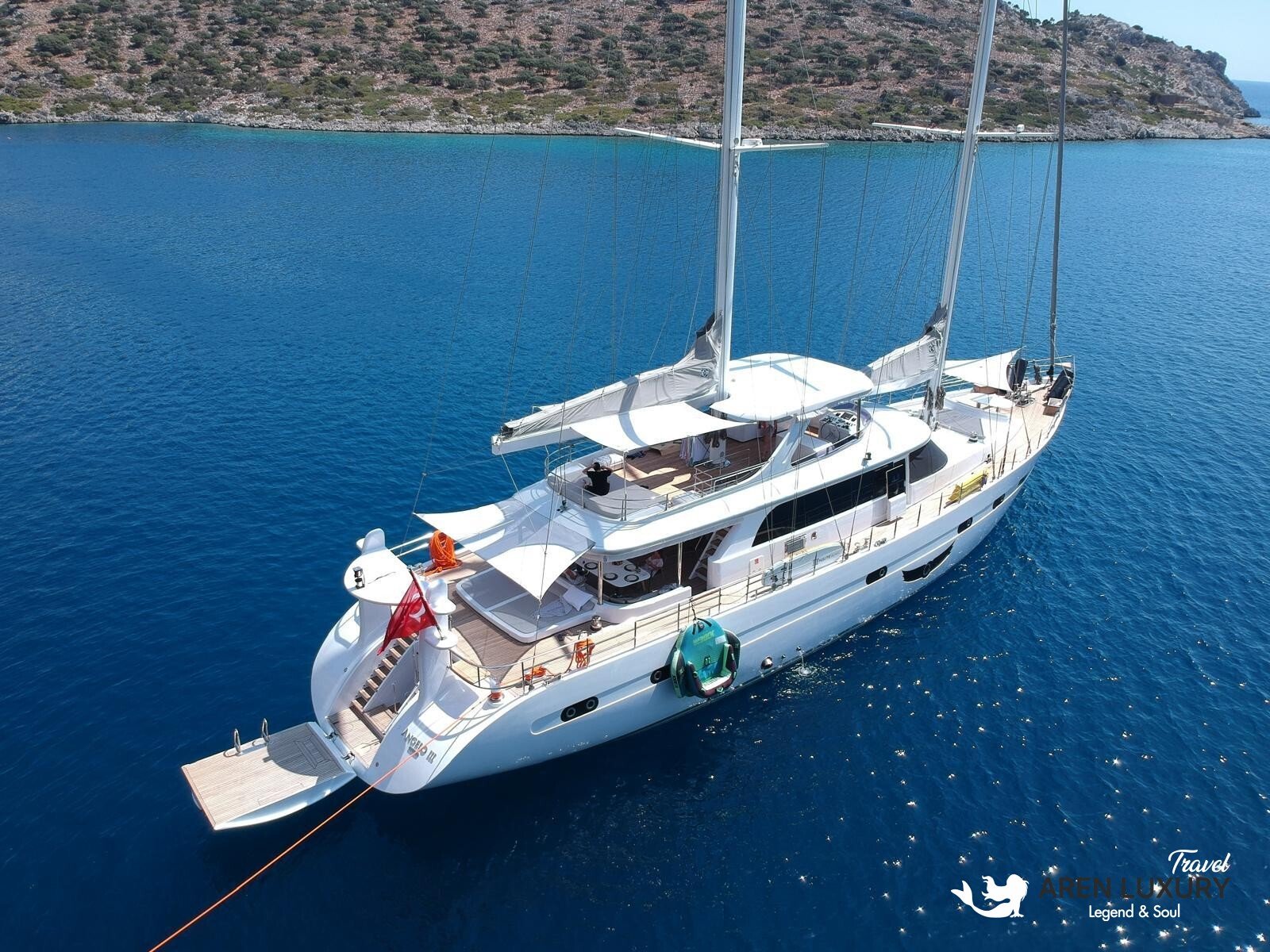 High-angle aerial view of the 35m Angelo 3 motorsailer yacht anchored in a deep blue Mediterranean bay.