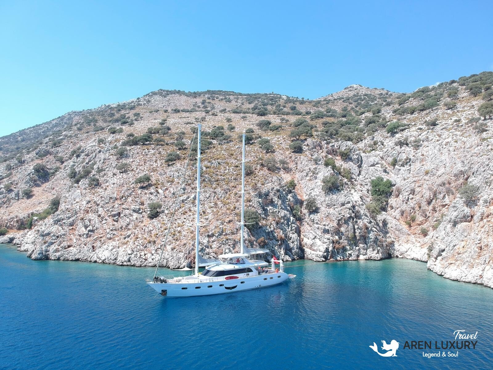 High-angle aerial view of the 35m Angelo 3 motorsailer yacht anchored in a deep blue Mediterranean bay.