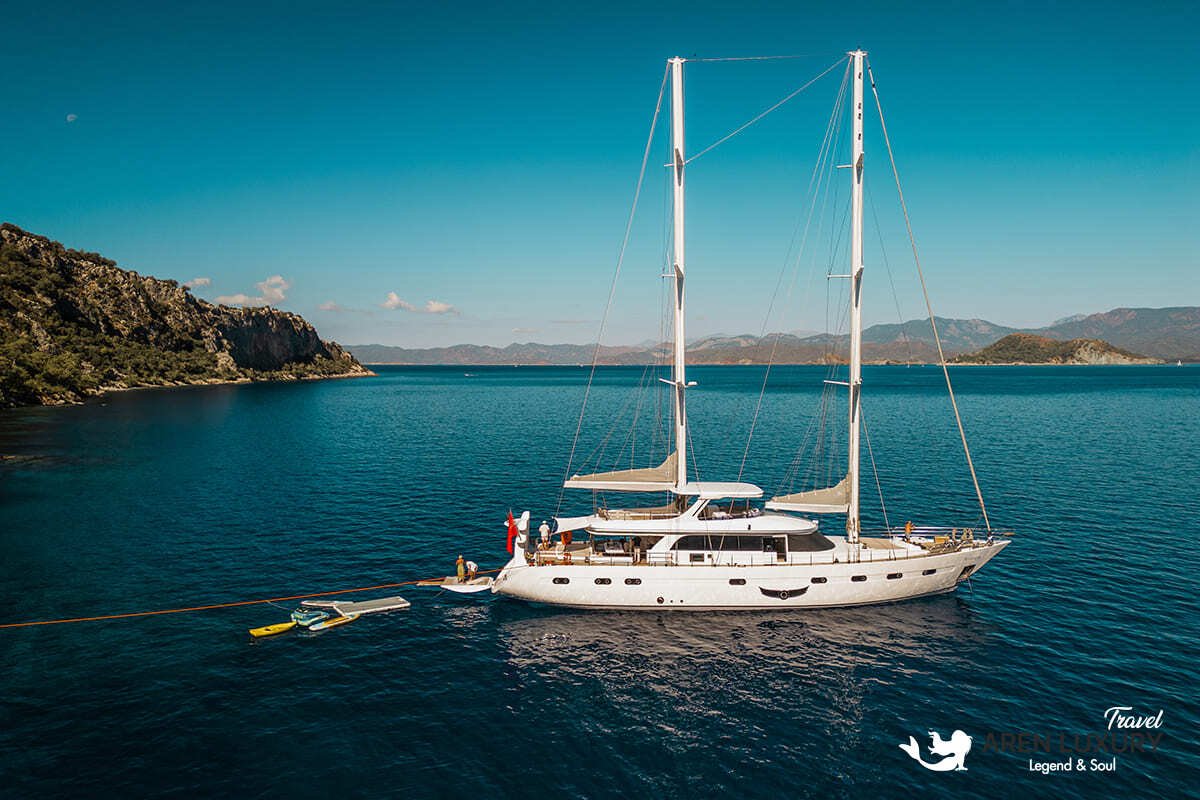 High-angle aerial view of the 35m Angelo 3 motorsailer yacht anchored in a deep blue Mediterranean bay.