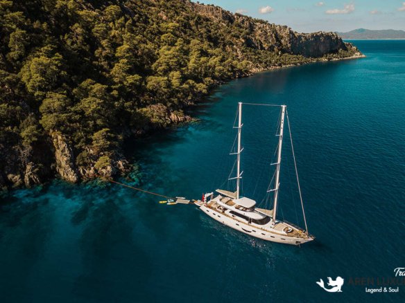 High-angle aerial view of the 35m Angelo 3 motorsailer yacht anchored in a deep blue Mediterranean bay.
