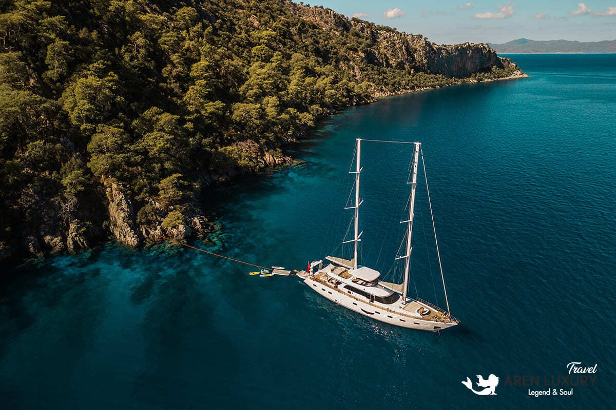 High-angle aerial view of the 35m Angelo 3 motorsailer yacht anchored in a deep blue Mediterranean bay.