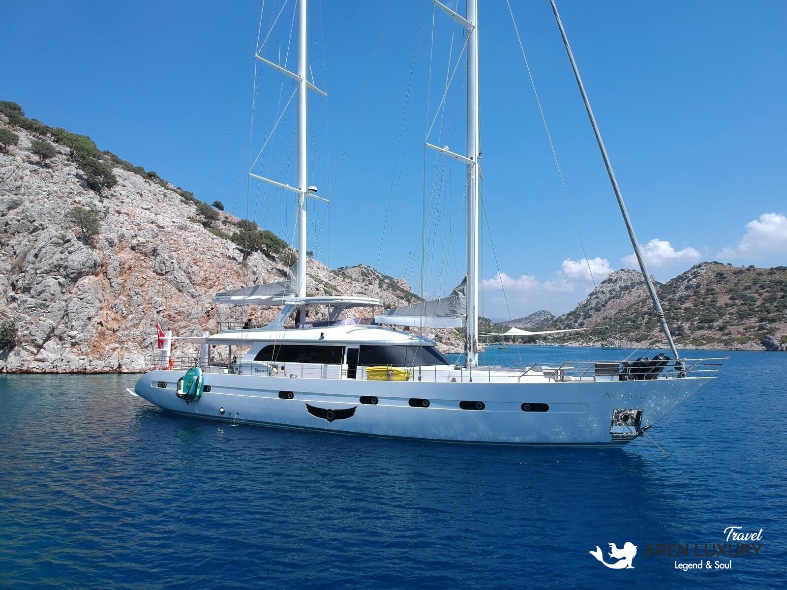 High-angle aerial view of the 35m Angelo 3 motorsailer yacht anchored in a deep blue Mediterranean bay.