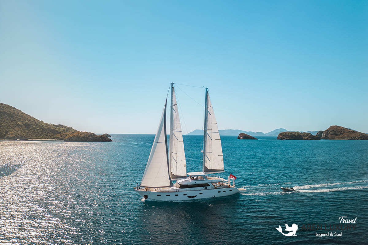 High-angle aerial view of the 35m Angelo 3 motorsailer yacht anchored in a deep blue Mediterranean bay.