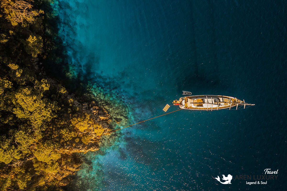 High-angle aerial view of the 35m Angelo 3 motorsailer yacht anchored in a deep blue Mediterranean bay.