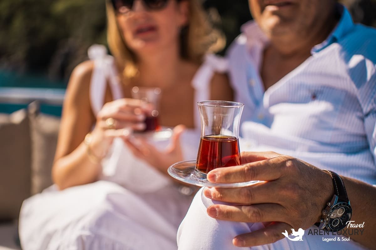 Side profile of the Angelo 3 motorsailer showing the sleek hull, flybridge, and dual masts against a coastal backdrop