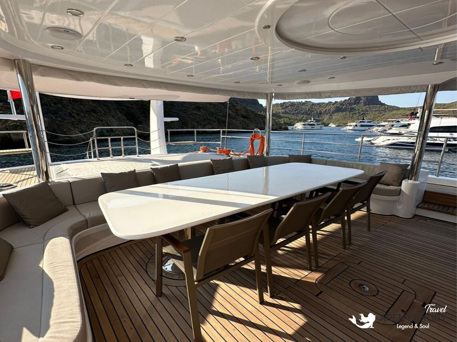 Side profile of the Angelo 3 motorsailer showing the sleek hull, flybridge, and dual masts against a coastal backdrop