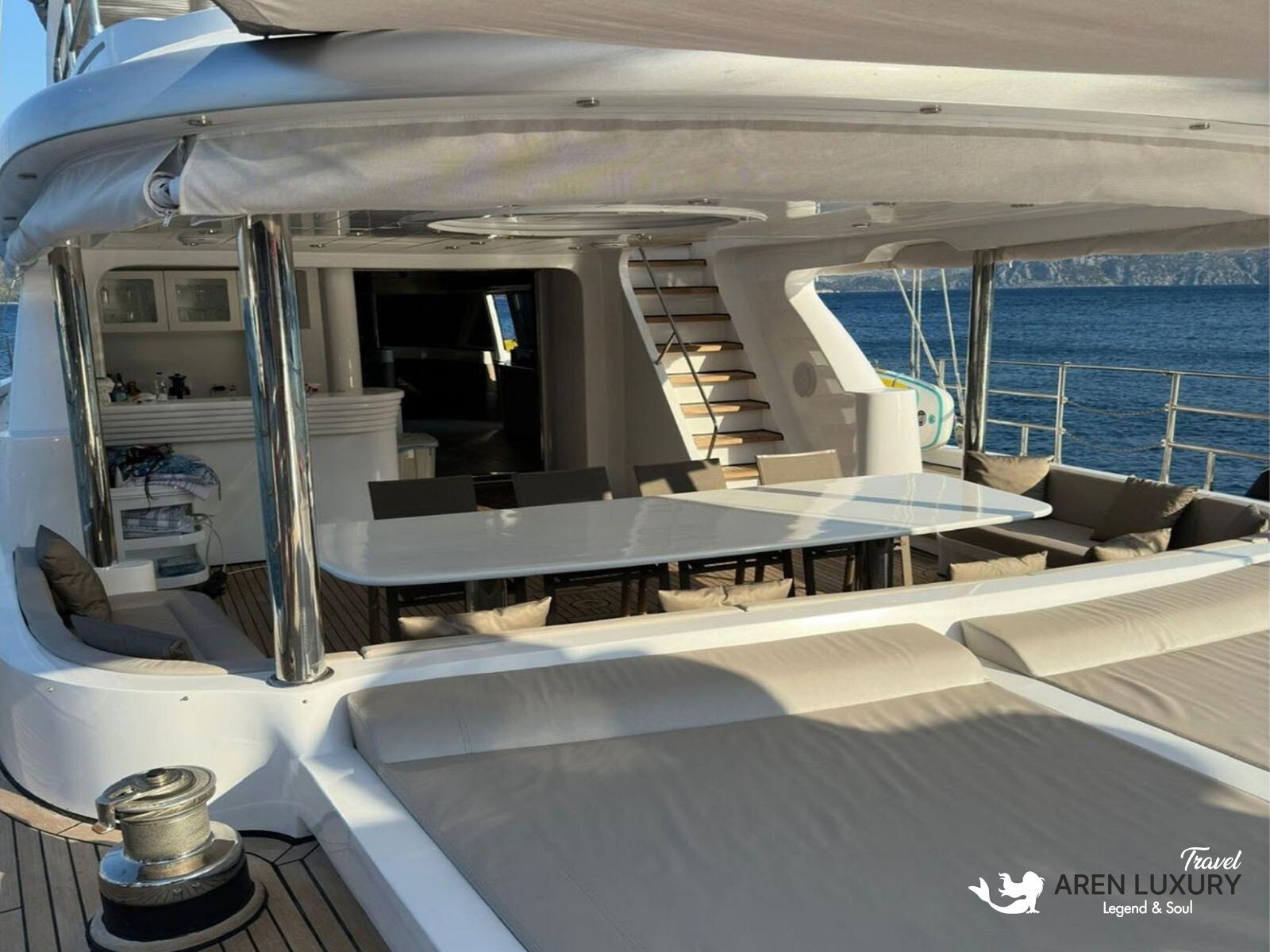 Side profile of the Angelo 3 motorsailer showing the sleek hull, flybridge, and dual masts against a coastal backdrop