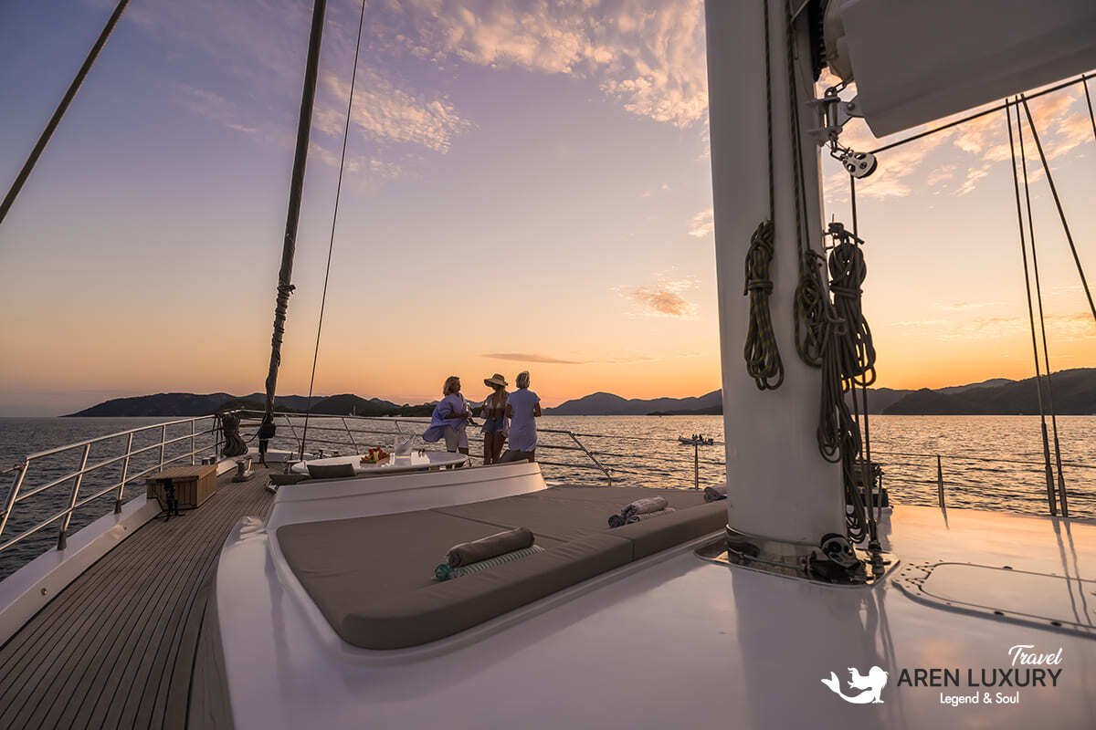 Aerial top-down view of Angelo 3 motorsailer with guests on the swim platform and various water toys in blue water.