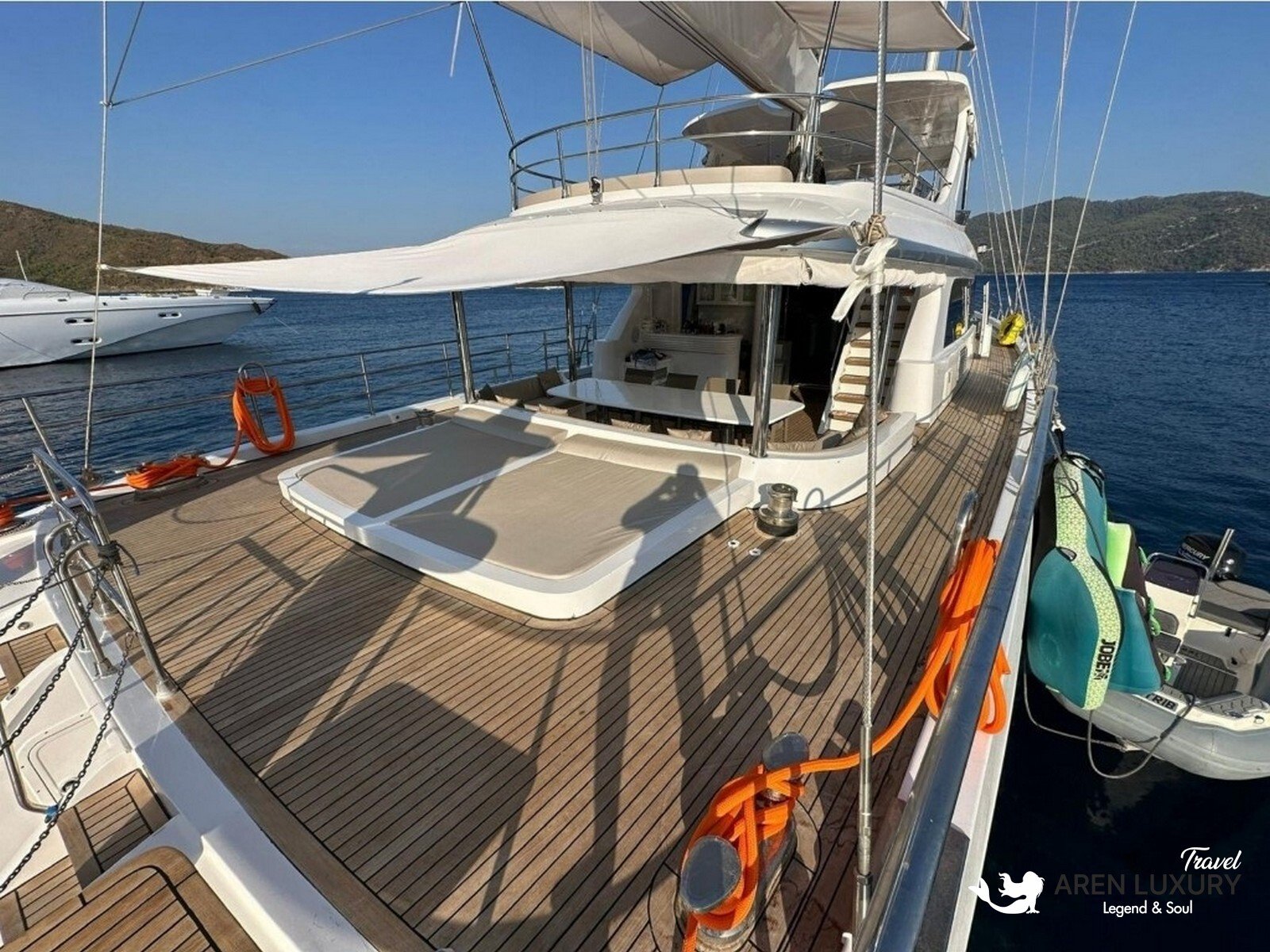 Side profile of the Angelo 3 motorsailer showing the sleek hull, flybridge, and dual masts against a coastal backdrop