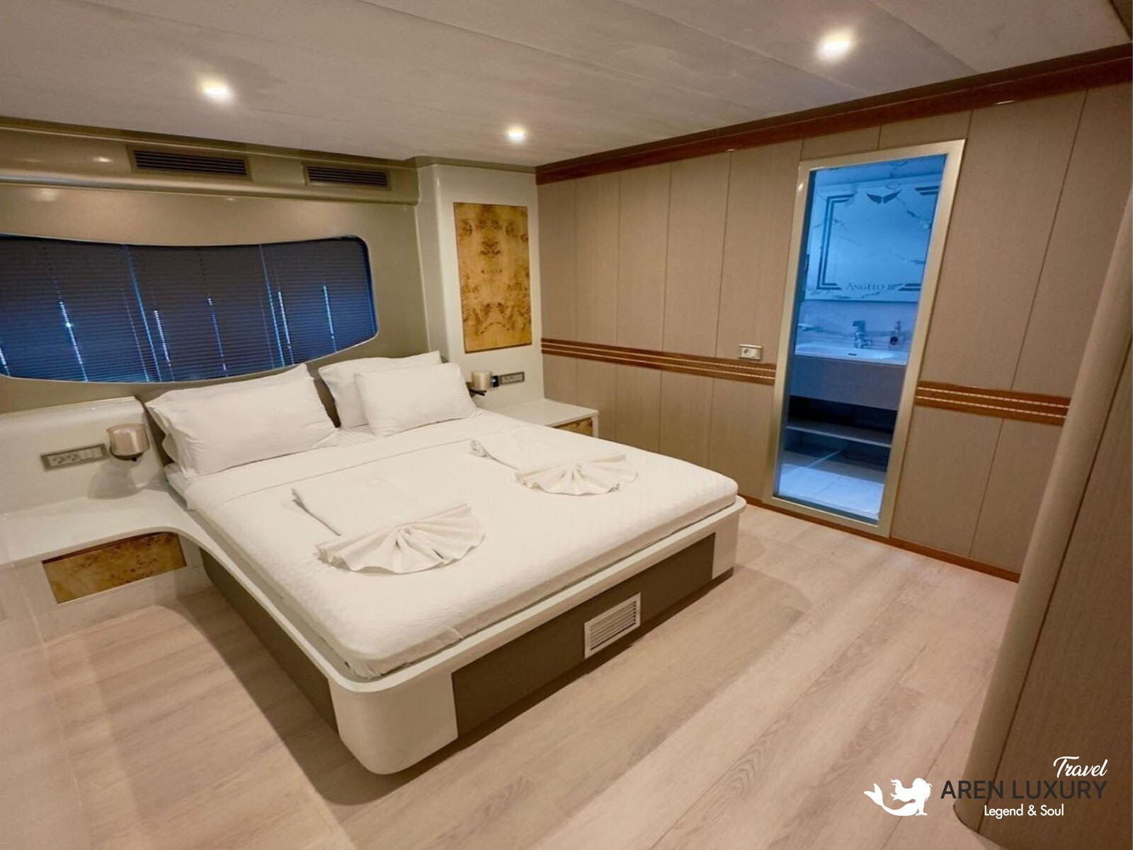 Modern luxury cabin interior of Angelo 3 motorsailer with a large bed, en-suite bathroom, and circular porthole window.