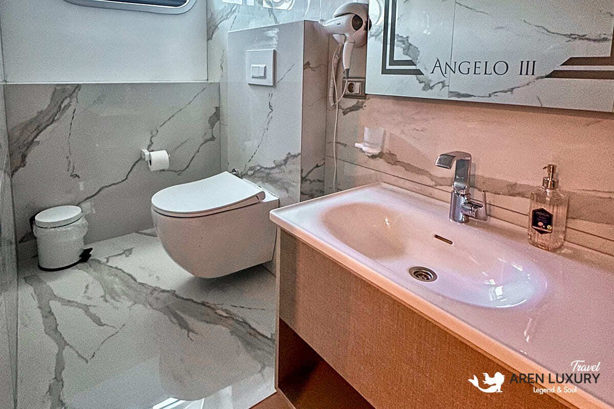 Modern luxury cabin interior of Angelo 3 motorsailer with a large bed, en-suite bathroom, and circular porthole window.