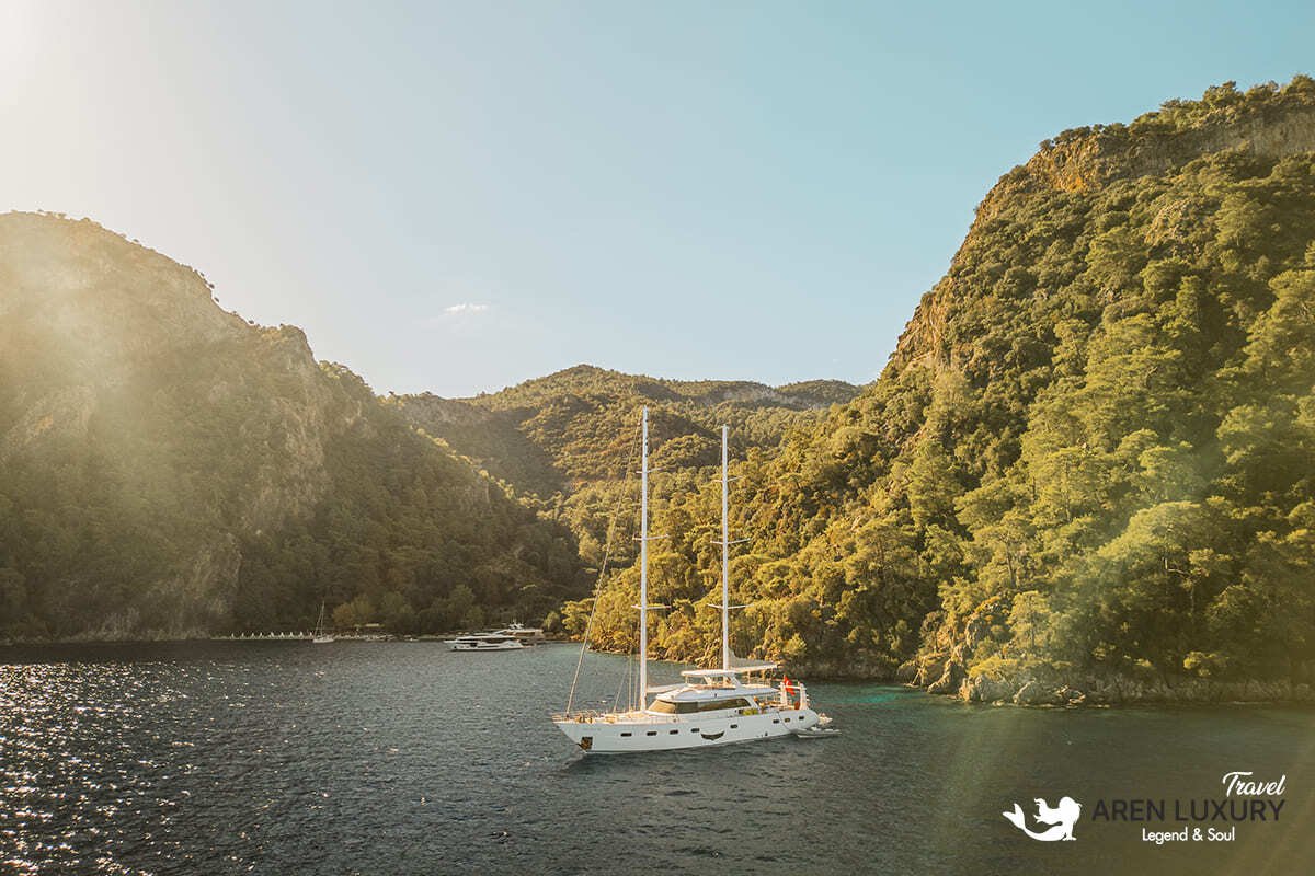 35-meter Angelo 3 motorsailer yacht navigating the crystal clear turquoise waters of a secluded Mediterranean cove.