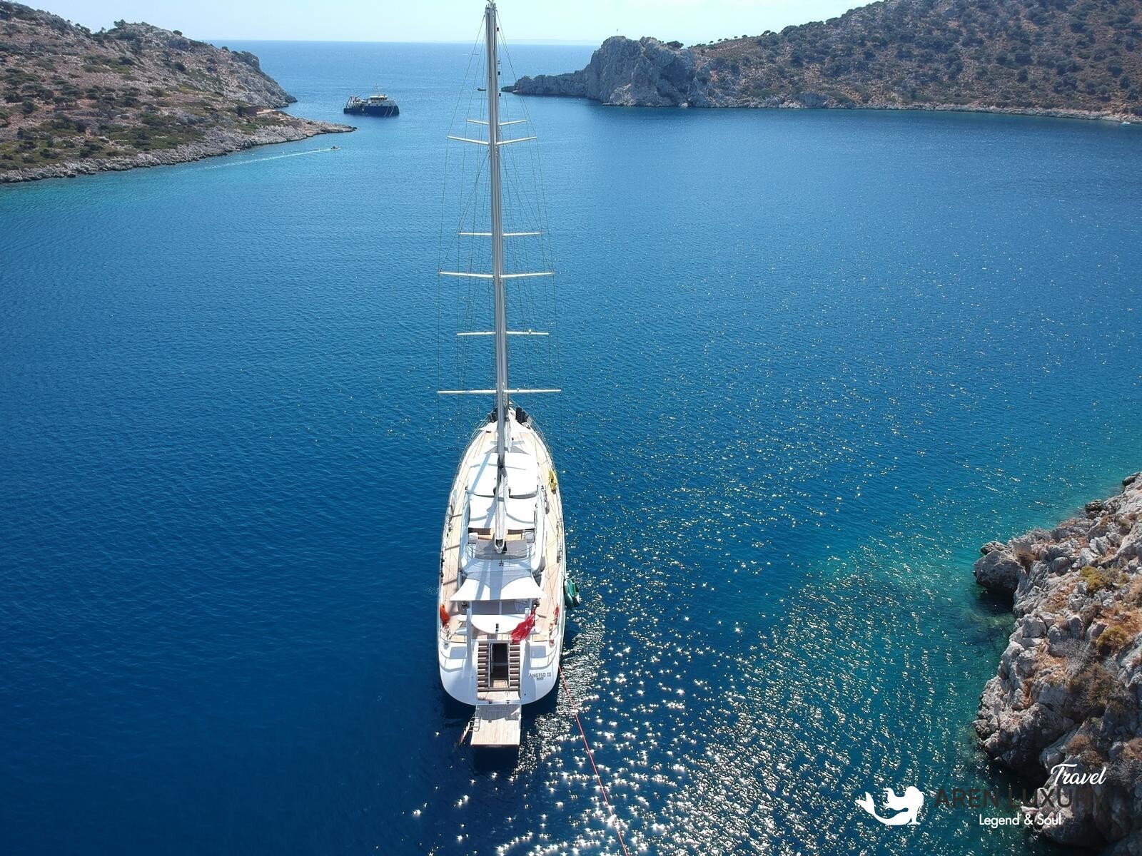 High-angle aerial view of the 35m Angelo 3 motorsailer yacht anchored in a deep blue Mediterranean bay.