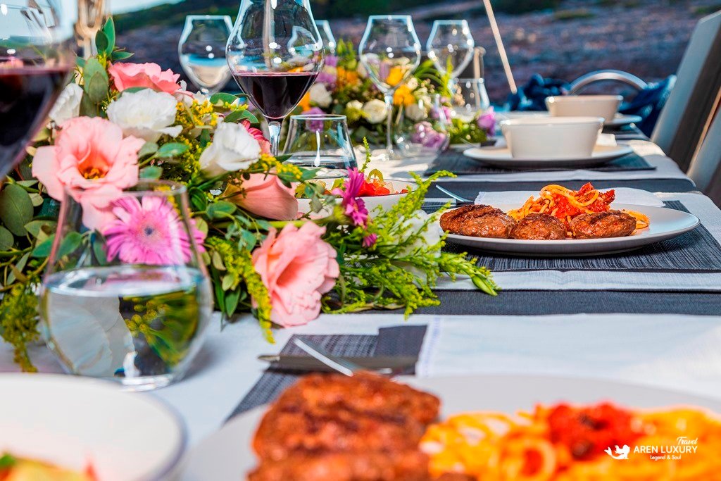 Gulet-Bodrum-Queen-Luxury-Catering-Detail Side view of a luxury yacht dining table featuring grilled meat dishes, wine glasses, and fresh floral arrangements.