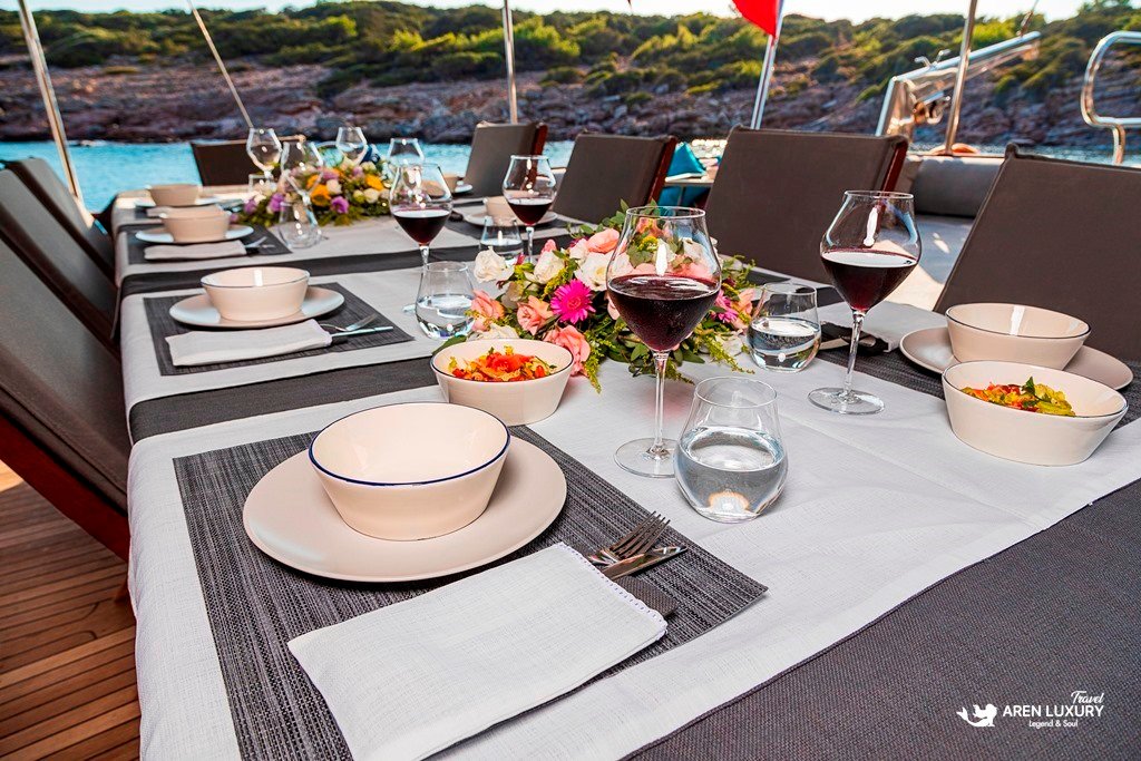 Elegant outdoor dining table with red wine glasses on the Bodrum Queen Gulet at sunset.