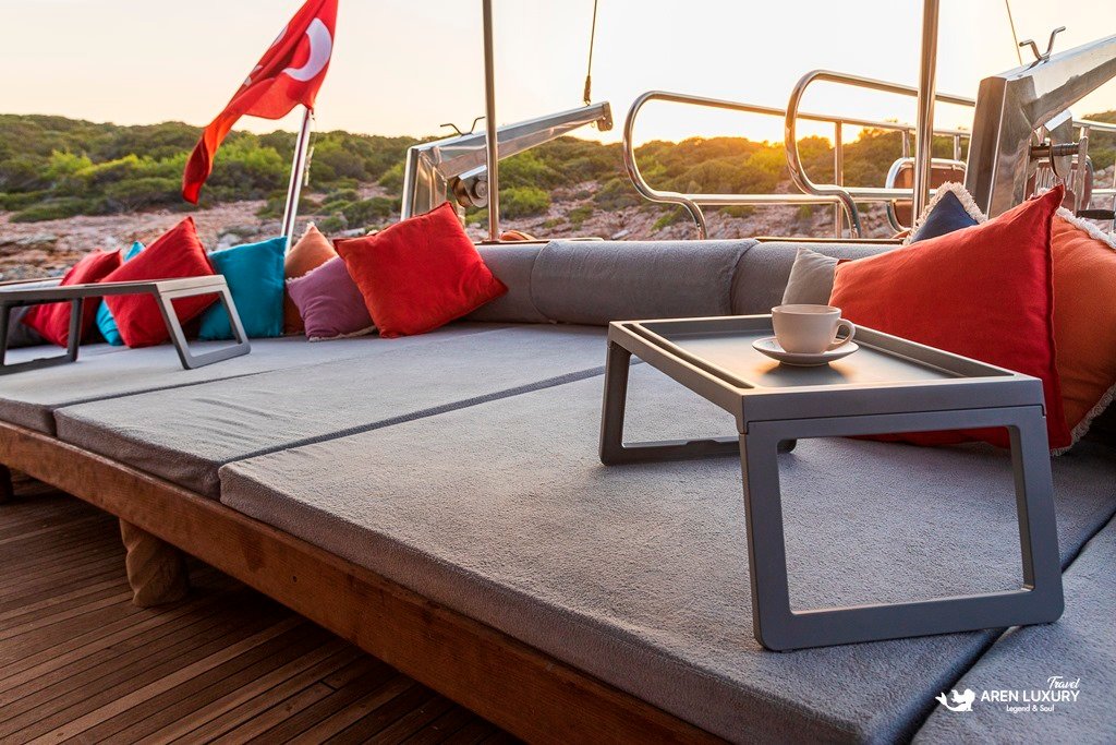 bodrum-queen-gulet-sunset-lounge-experience Luxury lounging area on the Bodrum Queen Gulet with red cushions and coffee trays at sunset.