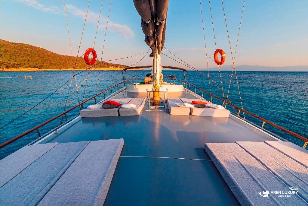 bodrum-queen-gulet-sailing-deck-view Spacious teak deck of the Bodrum Queen Gulet with sunbathing pads and life rings at sunset.