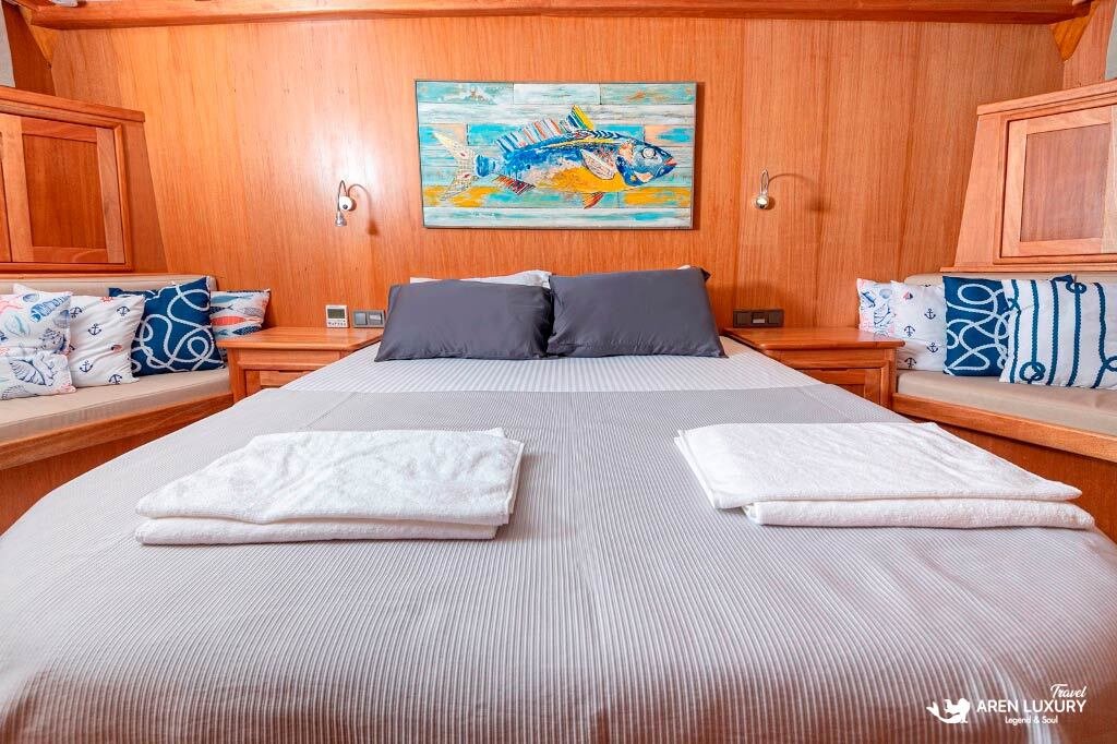 bodrum-queen-gulet-luxury-guest-cabin Luxury guest cabin on the Bodrum Queen Gulet featuring a large bed, warm wood interiors, and nautical fish artwork.