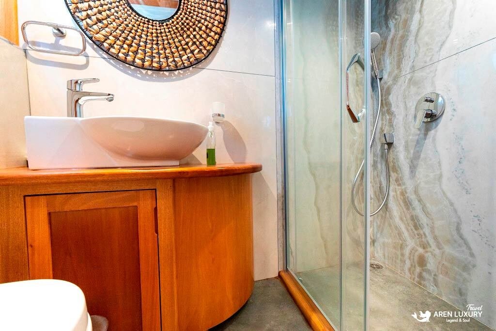 bodrum-queen-gulet-modern-bathroom-design Modern vessel ensuite on the Bodrum Queen Gulet featuring a round woven mirror and stone tiling.