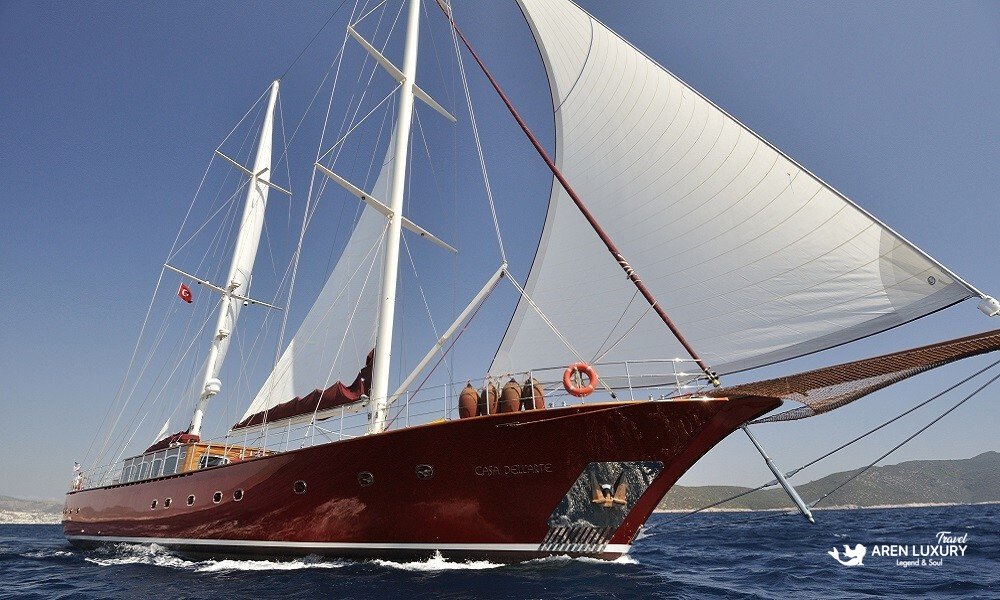 Full view of the Casa Dell'Arte 2 luxury gulet sailing in the Aegean Sea, showcasing its classic wooden hull and white sails under a clear blue sky.