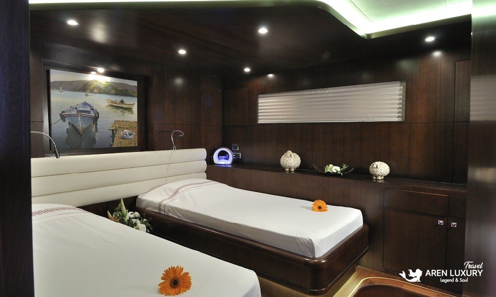 Casa-Dell-Arte-2-Gulet-Luxury-Twin-Cabin Boutique twin guest cabin on Casa Dell'Arte 2 luxury gulet, featuring two single beds with white linens, contemporary landscape art, and warm LED accent lighting.