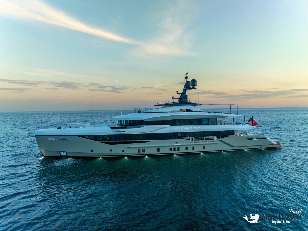 Exterior profile view of the luxury charter yacht Eternal Spark cruising on calm blue water at sunset.