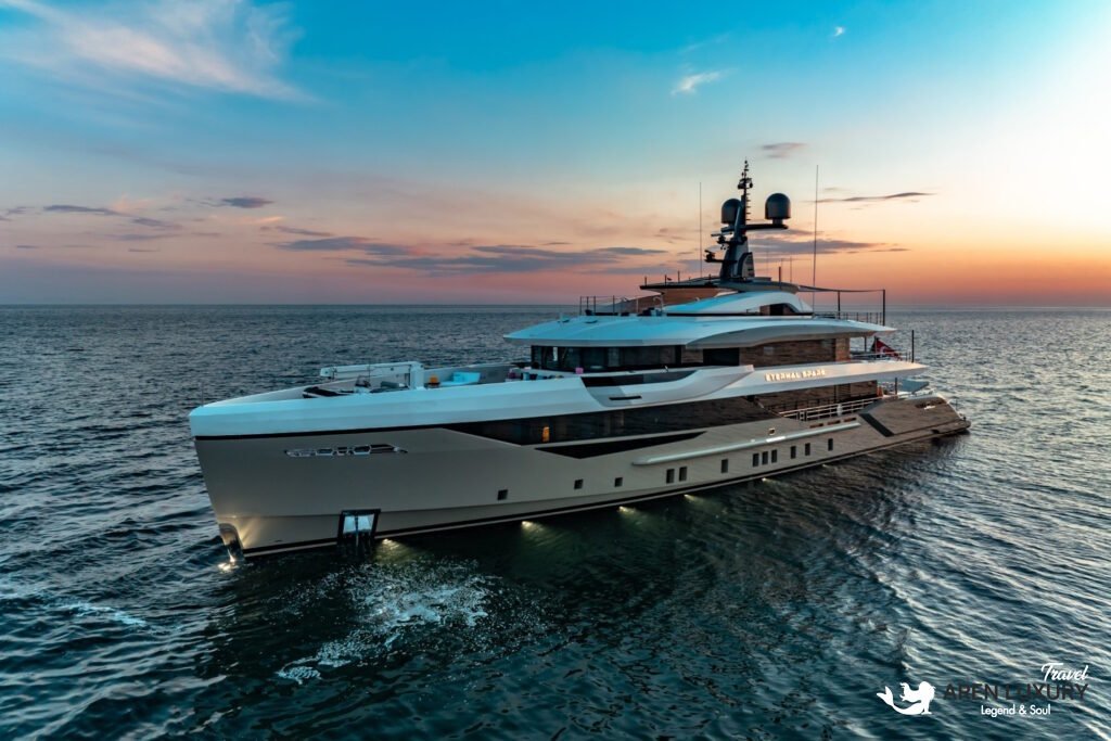 Full side profile of the luxury charter yacht Eternal Spark cruising on calm blue water under a bright sky.