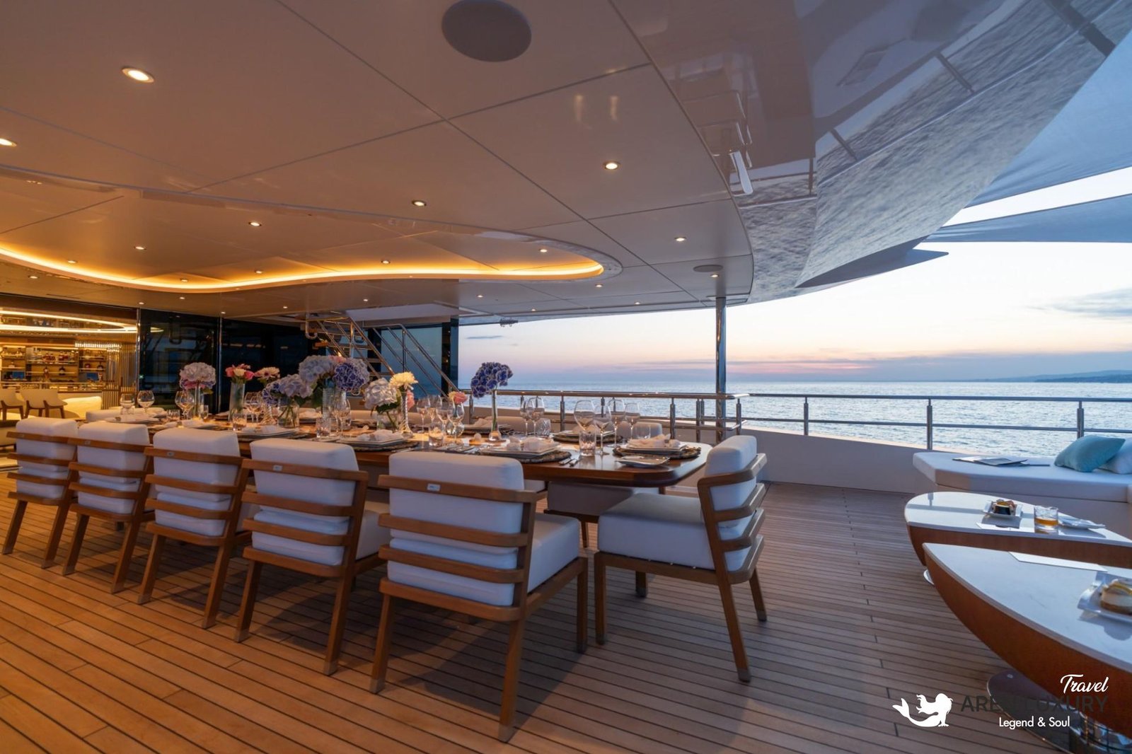 Elegant long dining table set for an evening meal on the illuminated teak deck of Eternal Spark yacht at sunset.