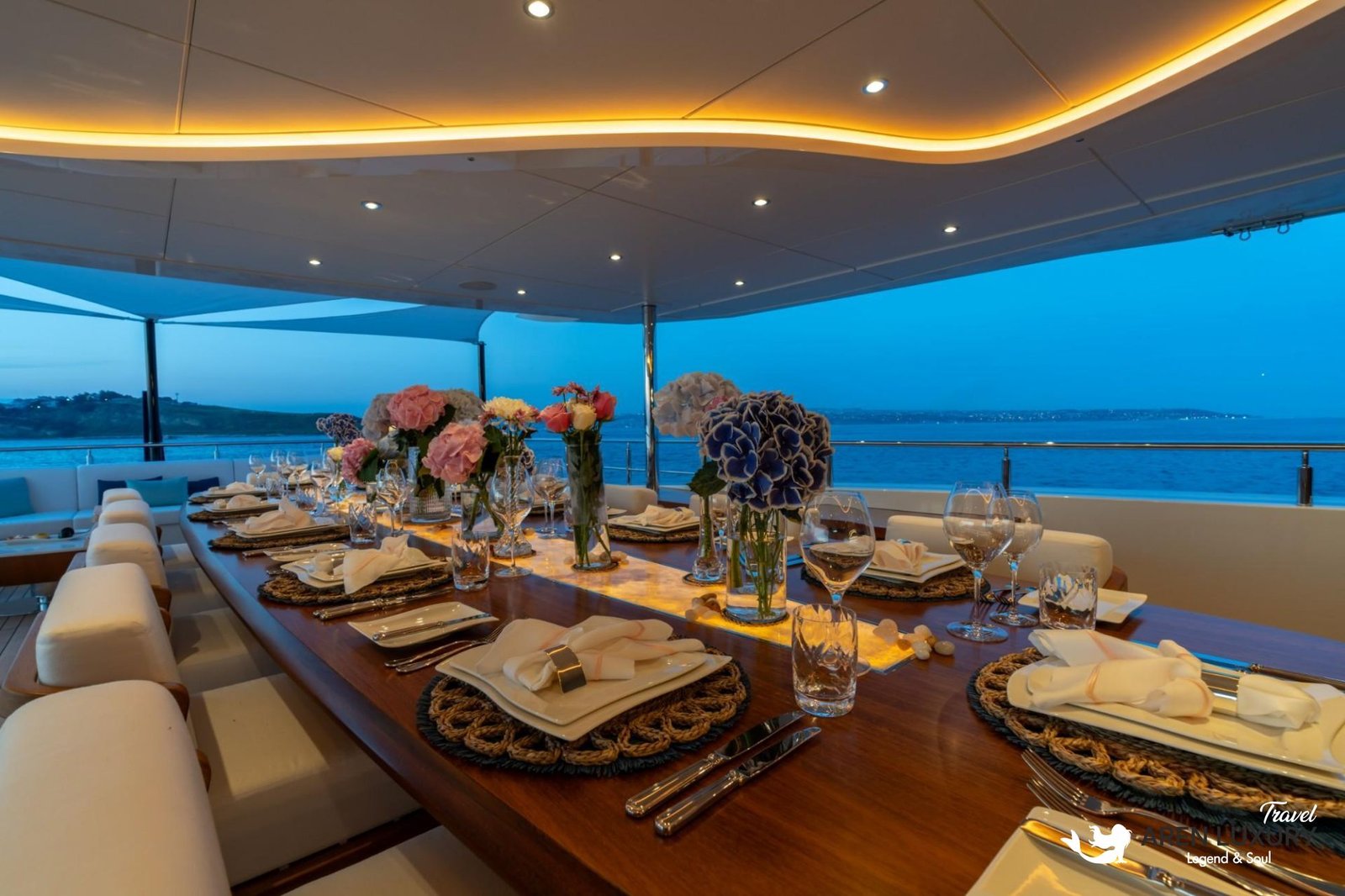 Close-up of a beautifully set long dining table on the teak deck of the charter yacht Eternal Spark at night with warm ambient lighting.