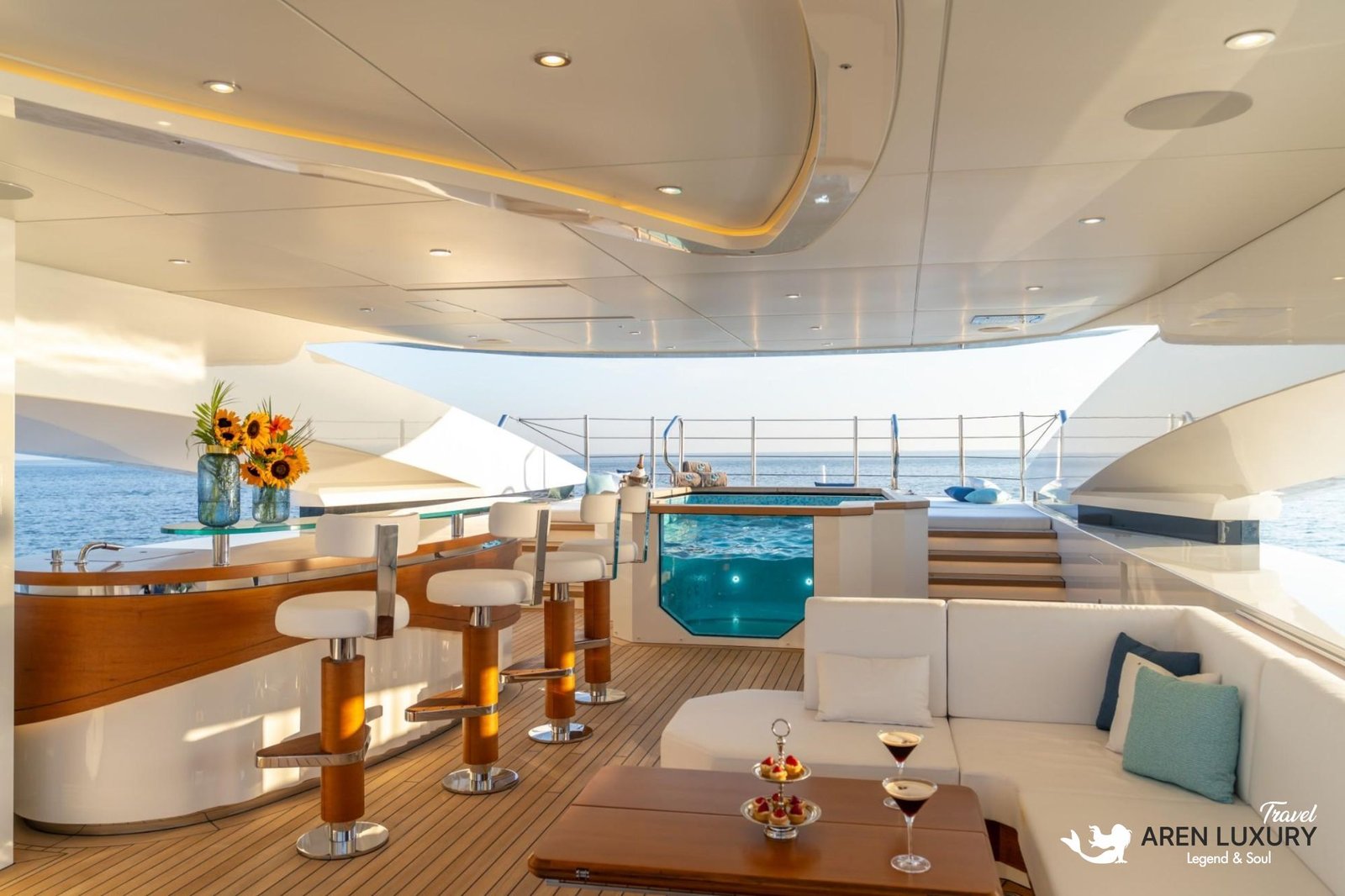 Luxurious sundeck bar on Eternal Spark yacht featuring a glass-walled plunge pool, modern bar stools, and comfortable lounge seating.