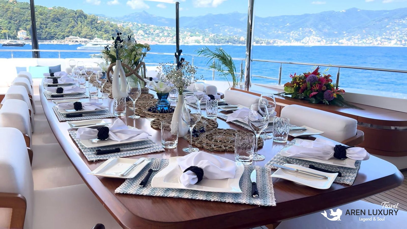 Elegant outdoor dining table set on the deck of charter yacht Eternal Spark with views of a Mediterranean coastline.