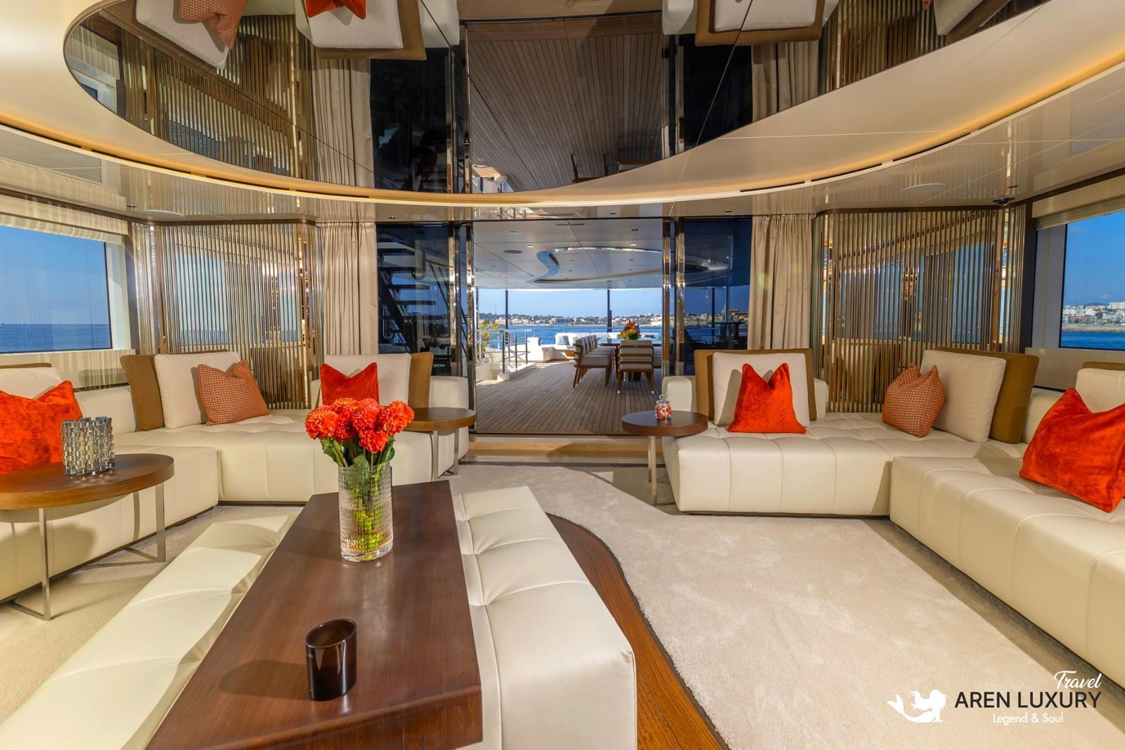 Modern luxury interior of the Eternal Spark yacht main salon featuring cream leather sofas, orange accent pillows, and large windows.