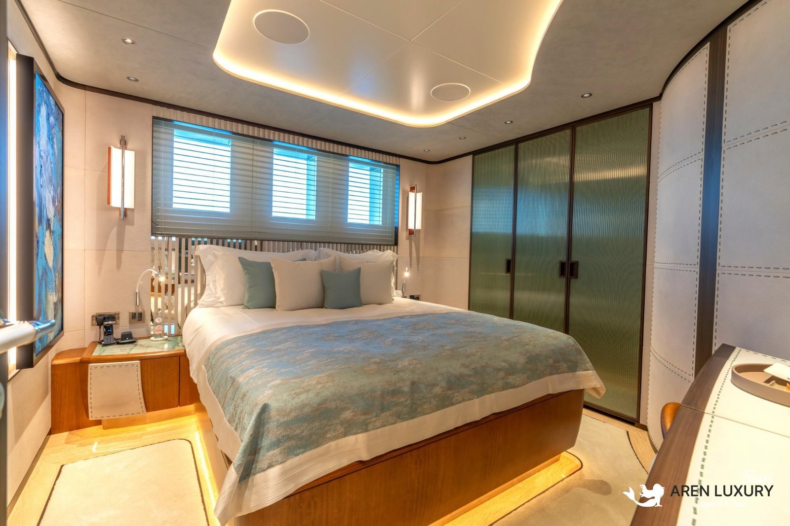 Modern luxury guest cabin on Eternal Spark yacht with a large double bed, ambient ceiling lighting, and blue textured artwork.