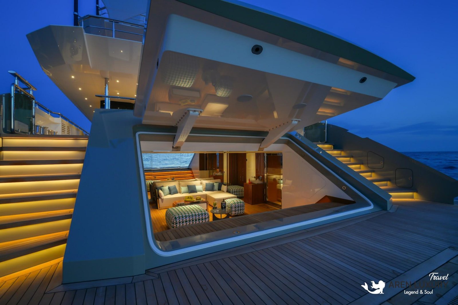 Illuminated beach club of Eternal Spark yacht at night, showing a lounge area with checkered ottomans and glowing stairs.