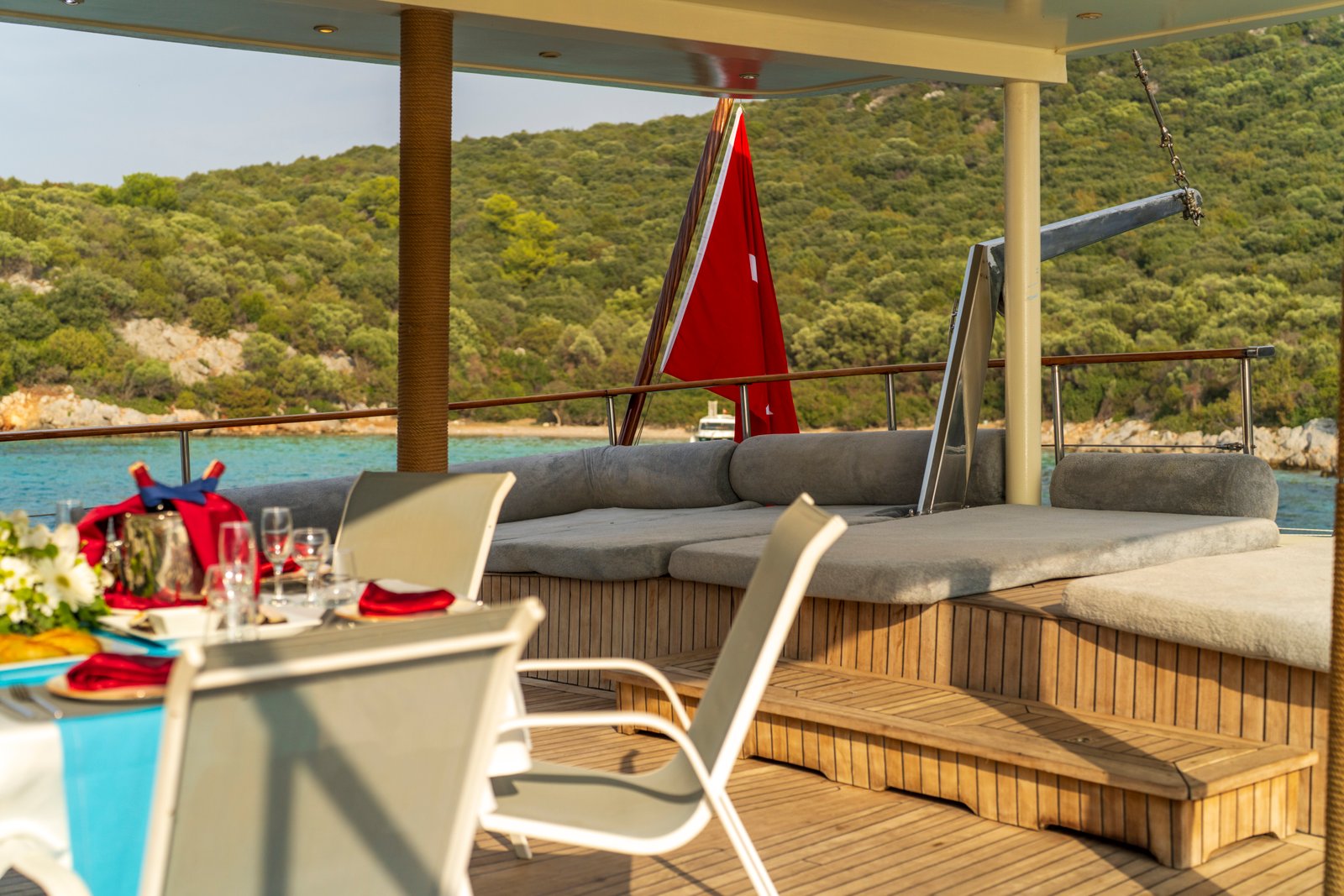 elara-1-gulet-aft-deck-lounge-seating Aft deck of the Elara 1 gulet featuring plush grey lounge cushions and a dining area overlooking the sea.