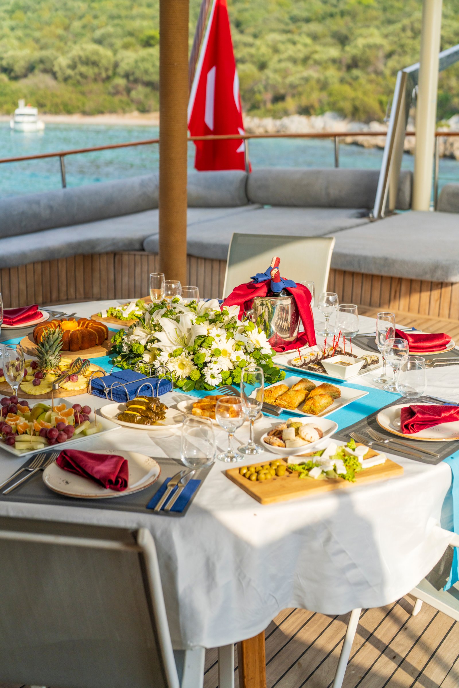 elara-1-gulet-dining-table-vertical Vertical view of an elegantly set outdoor dining table on the Elara 1 gulet with floral centerpieces and Mediterranean appetizers.