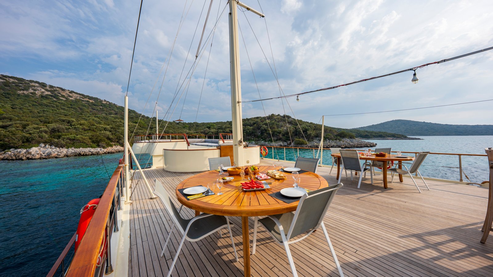 elara-1-gulet-dining-lifestyle Close-up of a circular wooden dining table on the Elara 1 gulet set with fresh fruit and appetizers.