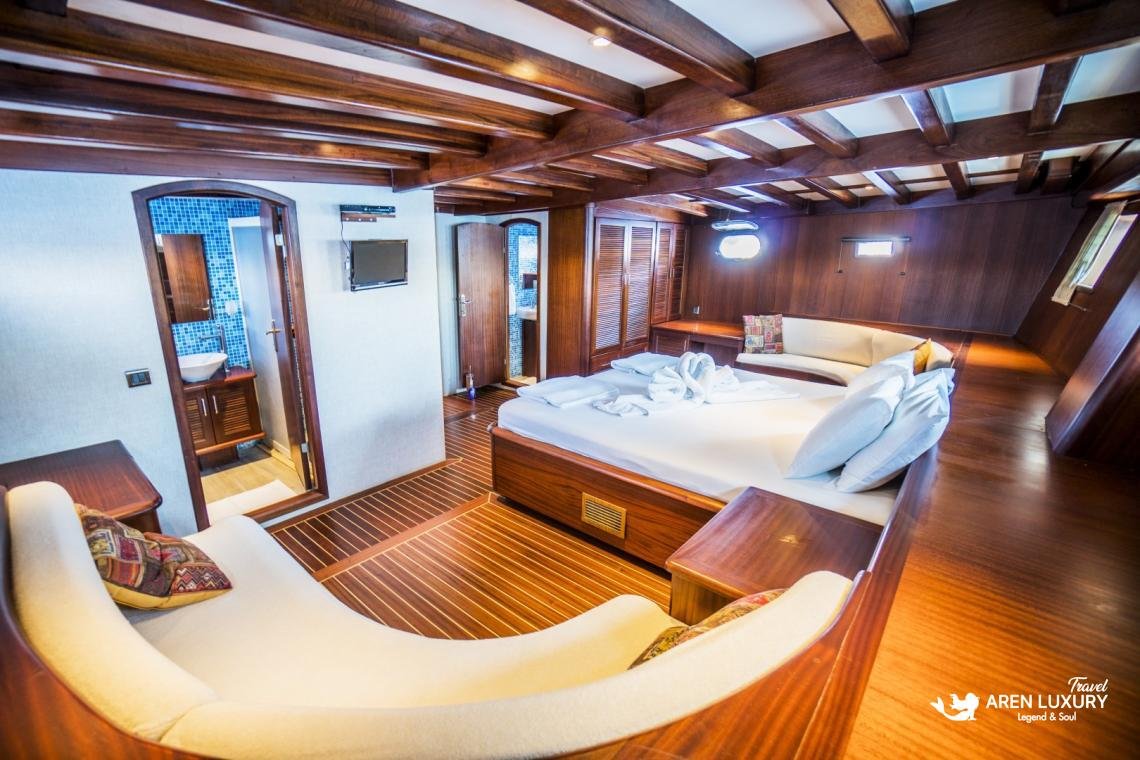 gulet-freedom-luxury-master-cabin-interior-bodrum Luxury master cabin on Gulet Freedom featuring a large double bed, curved white lounge sofa, and classic wood paneling with warm lighting.