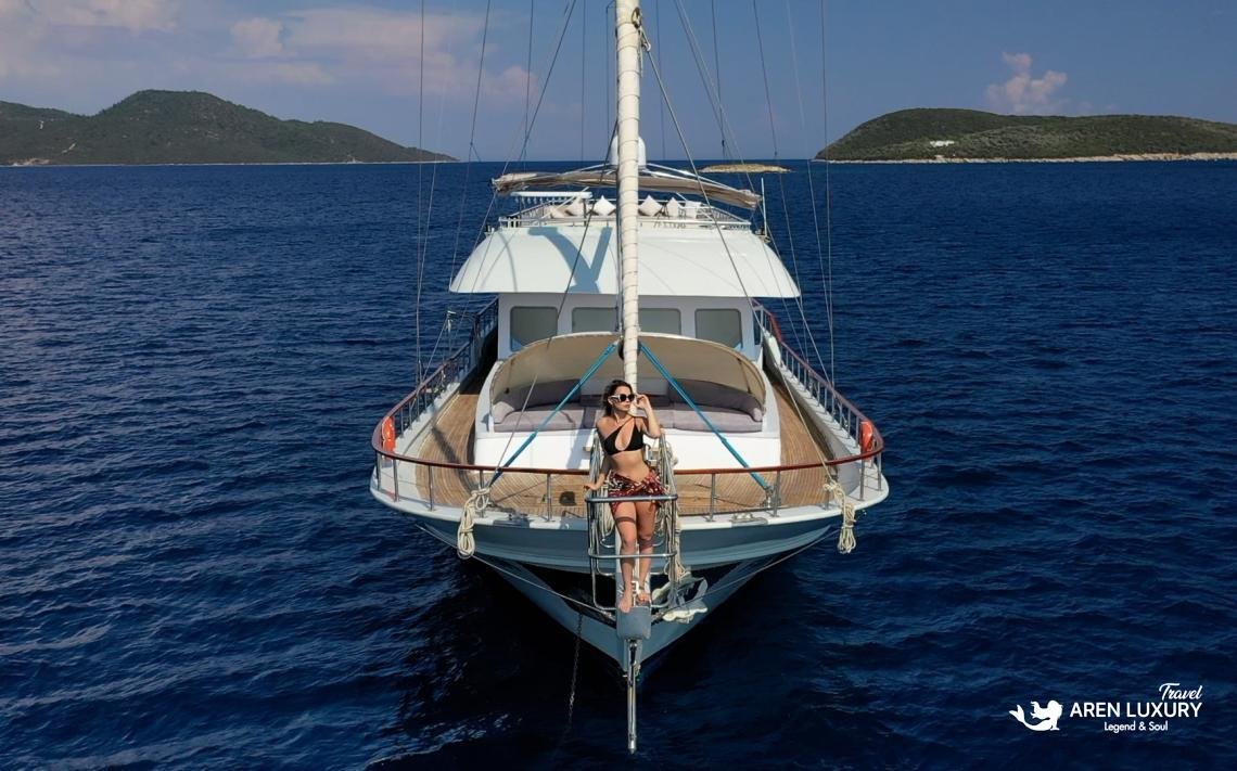 gulet-freedom-luxury-charter-foredeck-sun-pads Luxury ketch Gulet Freedom at sea with a guest relaxing on the foredeck sun pads under a white canopy.
