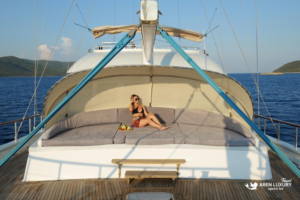 gulet-freedom-luxury-foredeck-sunbathing-area A guest relaxing on large grey sunpads under a white shaded canopy on the foredeck of Gulet Freedom.