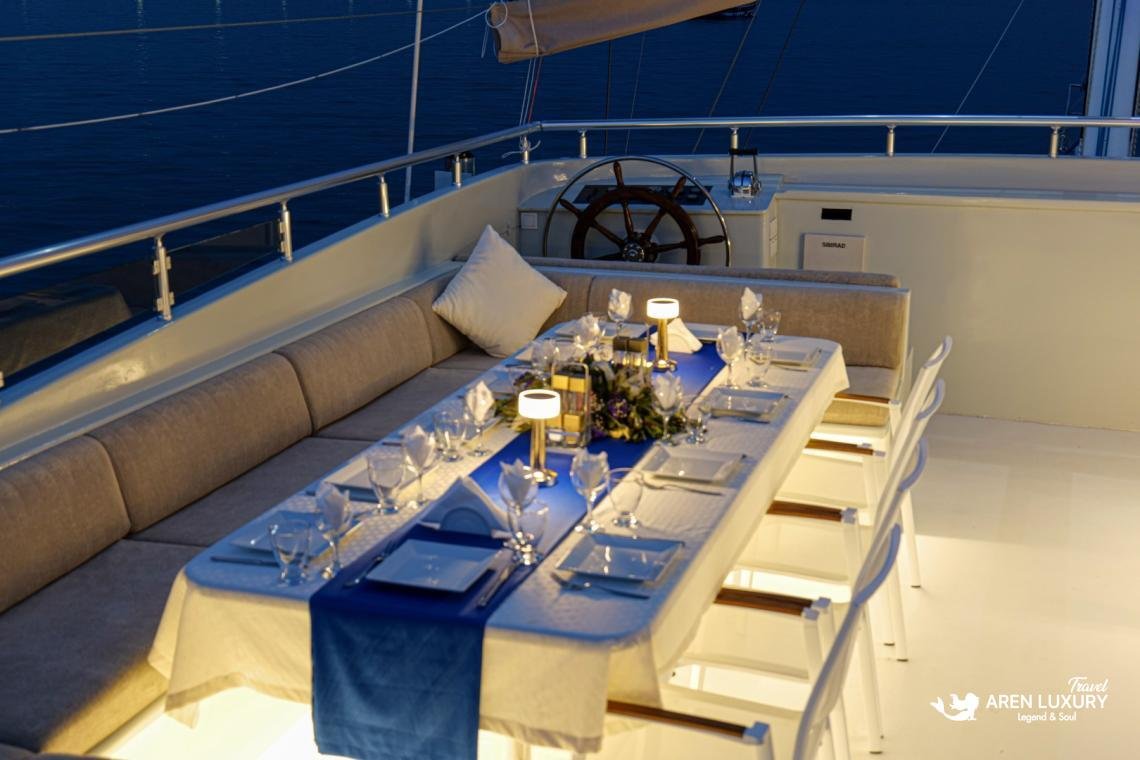 gulet-freedom-luxury-aft-deck-night-dining Elegantly set outdoor dining table on the aft deck of Gulet Freedom at night, featuring blue runners, warm candles, and white linens.