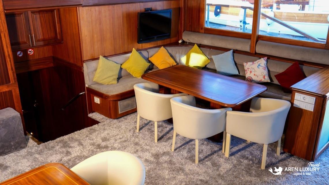 gulet-freedom-luxury-yacht-saloon-interior-bodrum Luxury interior saloon of Gulet Freedom featuring a large wooden dining table, plush grey seating, and modern nautical decor.