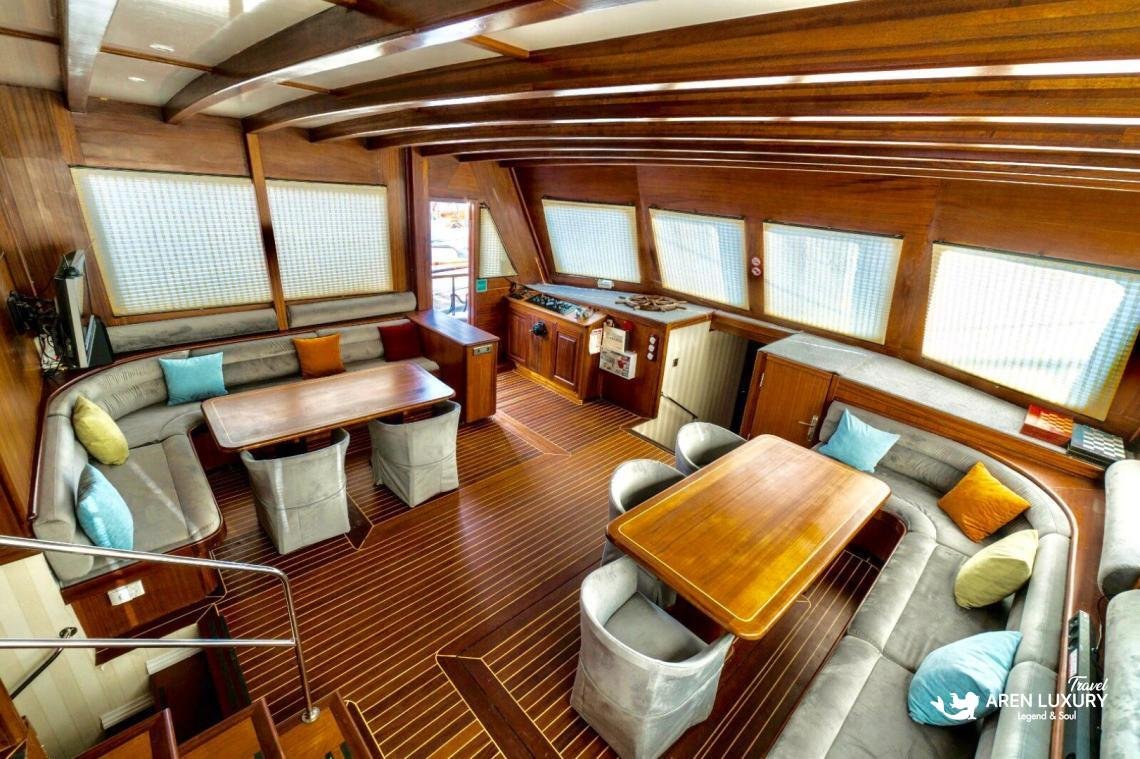 gulet-freedom-luxury-saloon-interior-design Spacious luxury saloon of Gulet Freedom featuring warm wood finishes, twin dining tables, and plush grey seating.