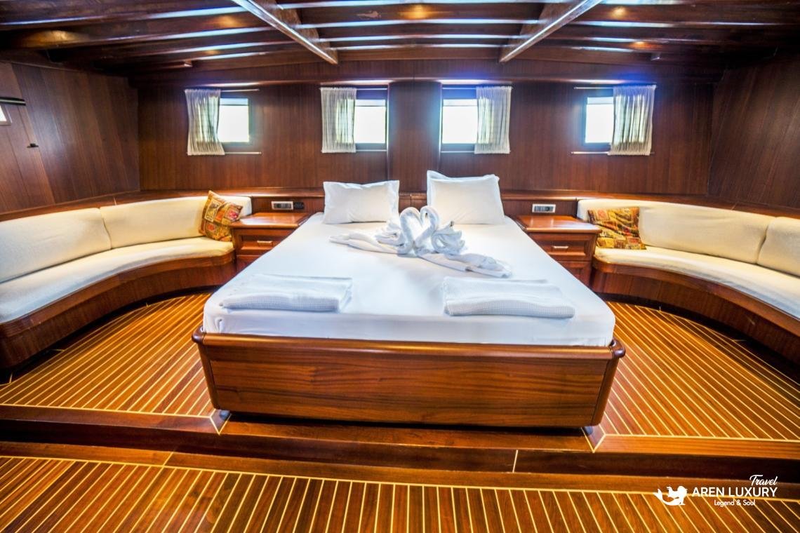 gulet-freedom-luxury-master-cabin-interior Spacious luxury master cabin on Gulet Freedom featuring a large double bed, polished wood flooring, and curved lounge seating.