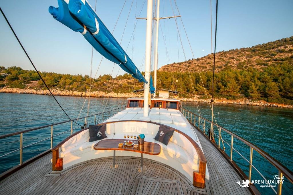 Curved luxury forward deck lounge on Gulet Gokce at sunset with a polished wooden table and panoramic Mediterranean views.