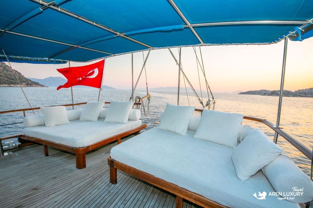 Spacious aft deck sun lounge on Gulet Gokce featuring large white sunbeds under a blue awning with a Turkish flag.