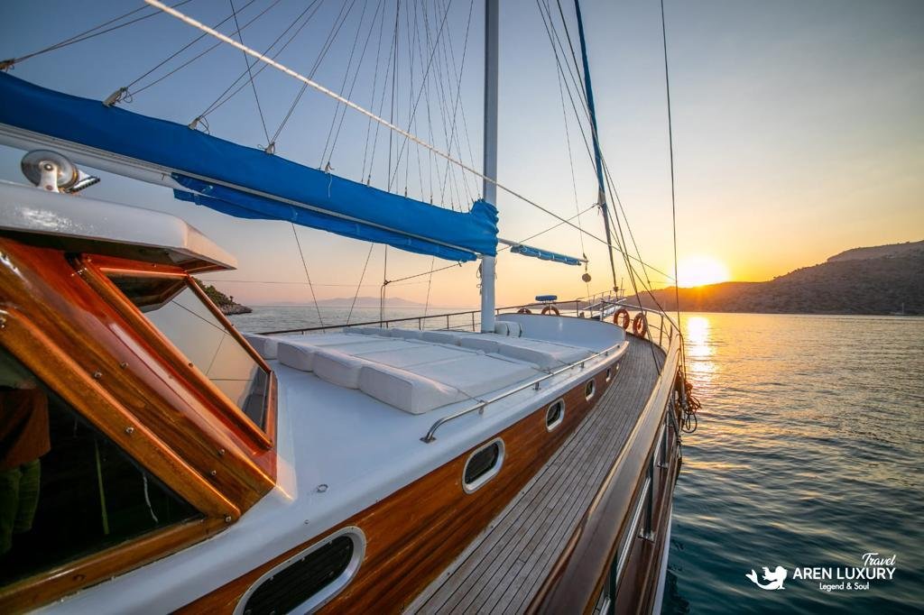 Side deck view of Gulet Gokce at sunset with polished wooden hull details and white sunbathing cushions under a clear sky.