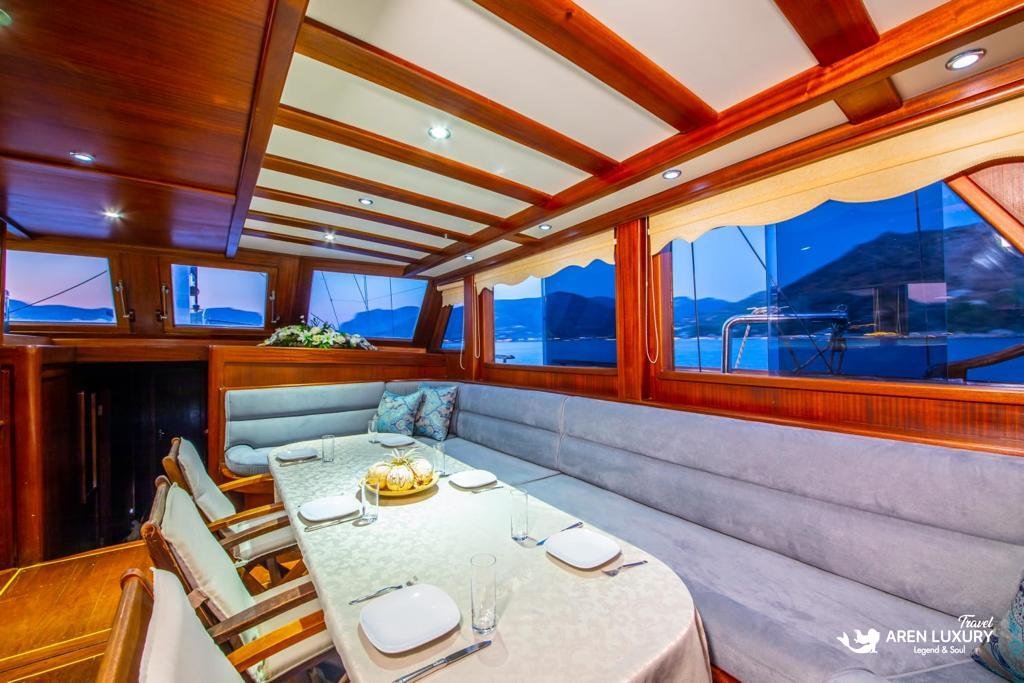 Luxury indoor dining salon of Gulet Gokce featuring a long dining table, plush grey seating, and large windows with sea views.
