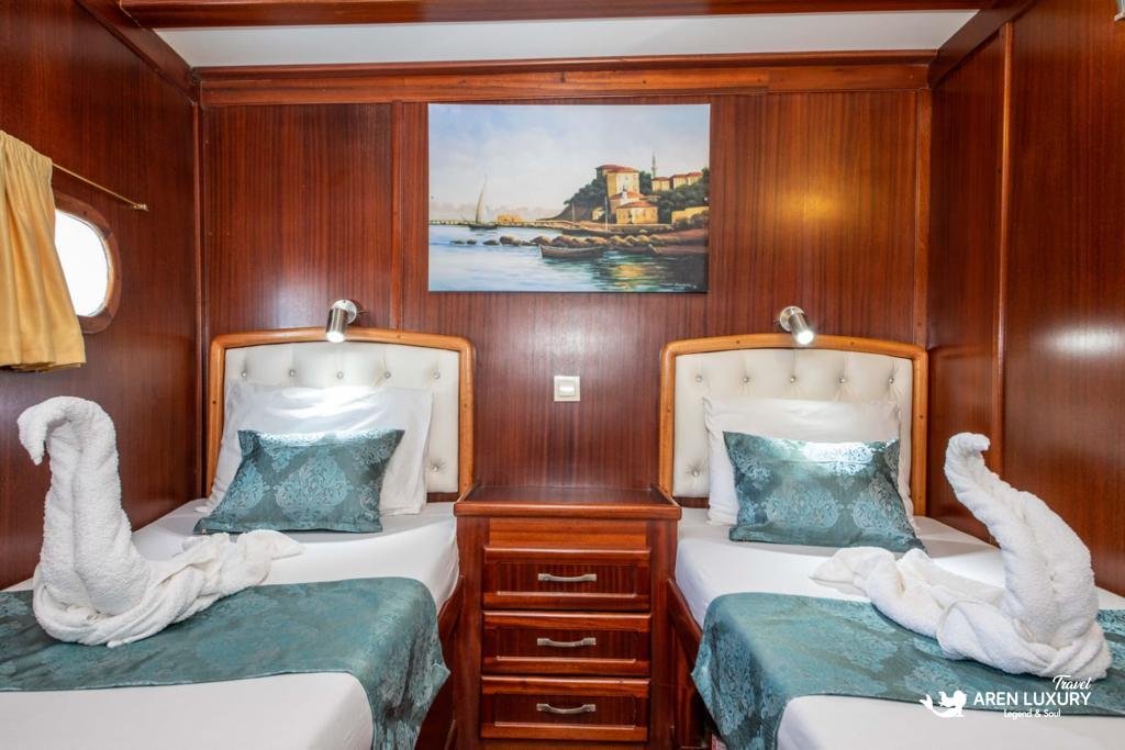 Luxury twin guest cabin on Gulet Gokce featuring two single beds, mahogany paneling, and a decorative nautical painting.