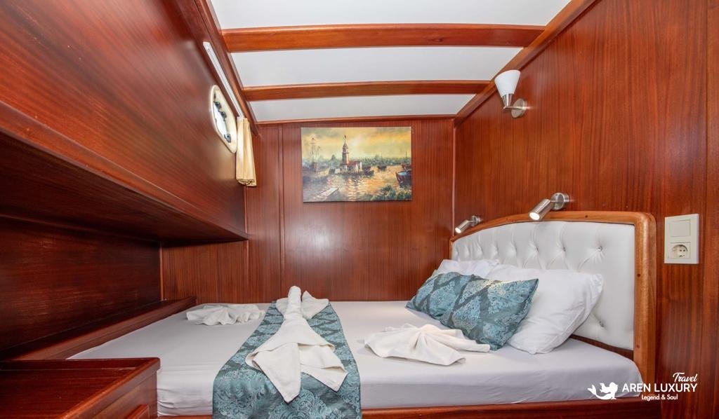 Traditional mahogany double cabin on Gulet Gokce with white quilted headboard and a coastal landscape painting.